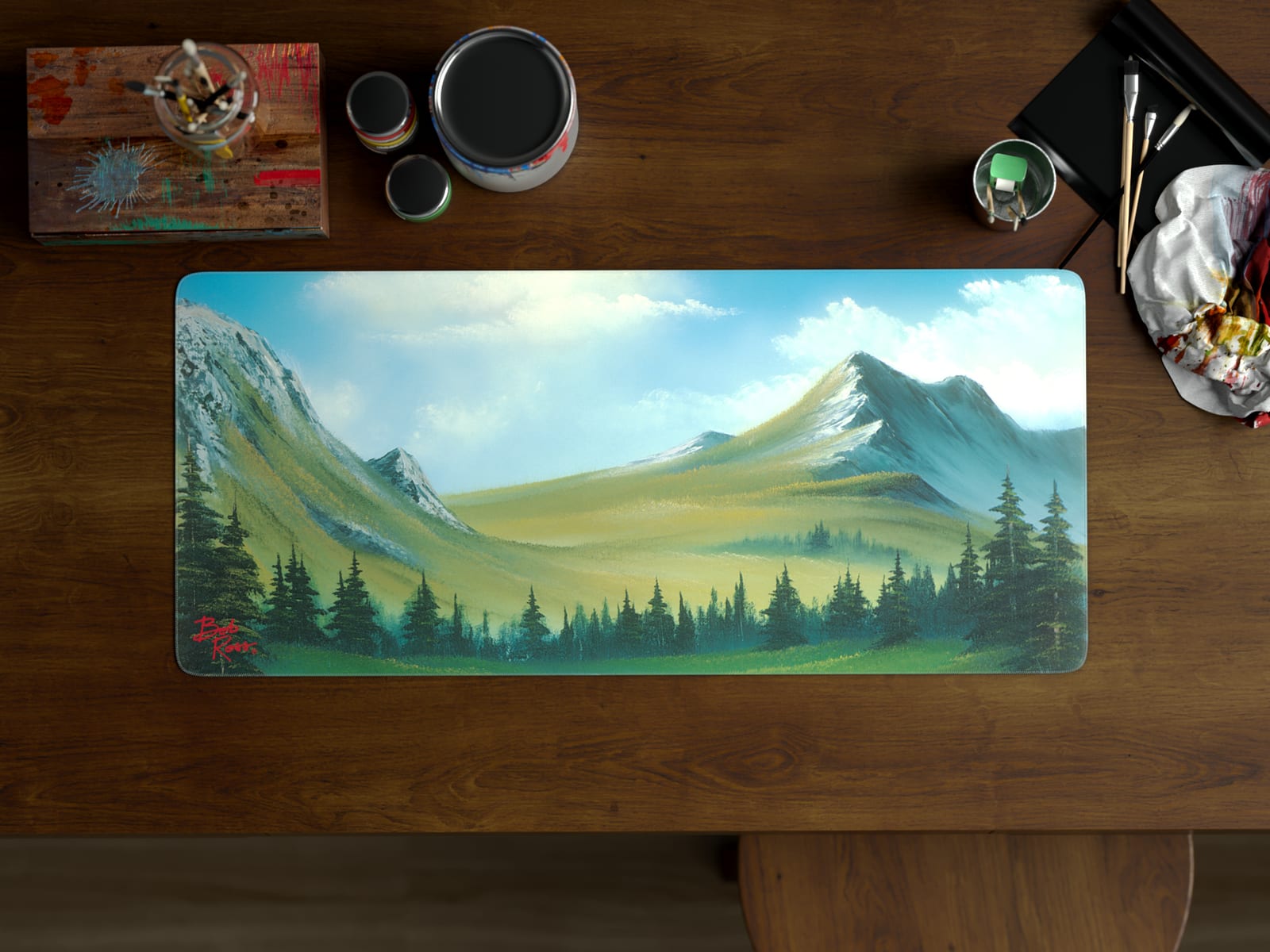 Bob Ross deskmat with a mountain landscape painting on a wooden desk