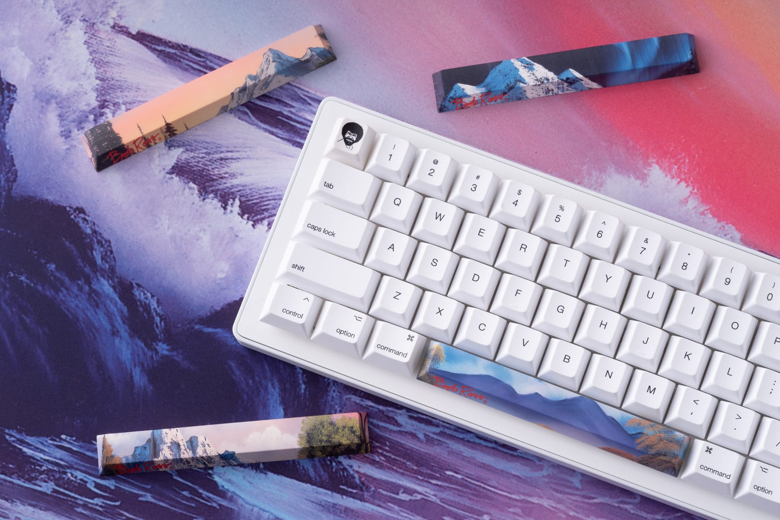 Apos x Bob Ross panoramic scenic keycaps next to a white mechanical keyboard